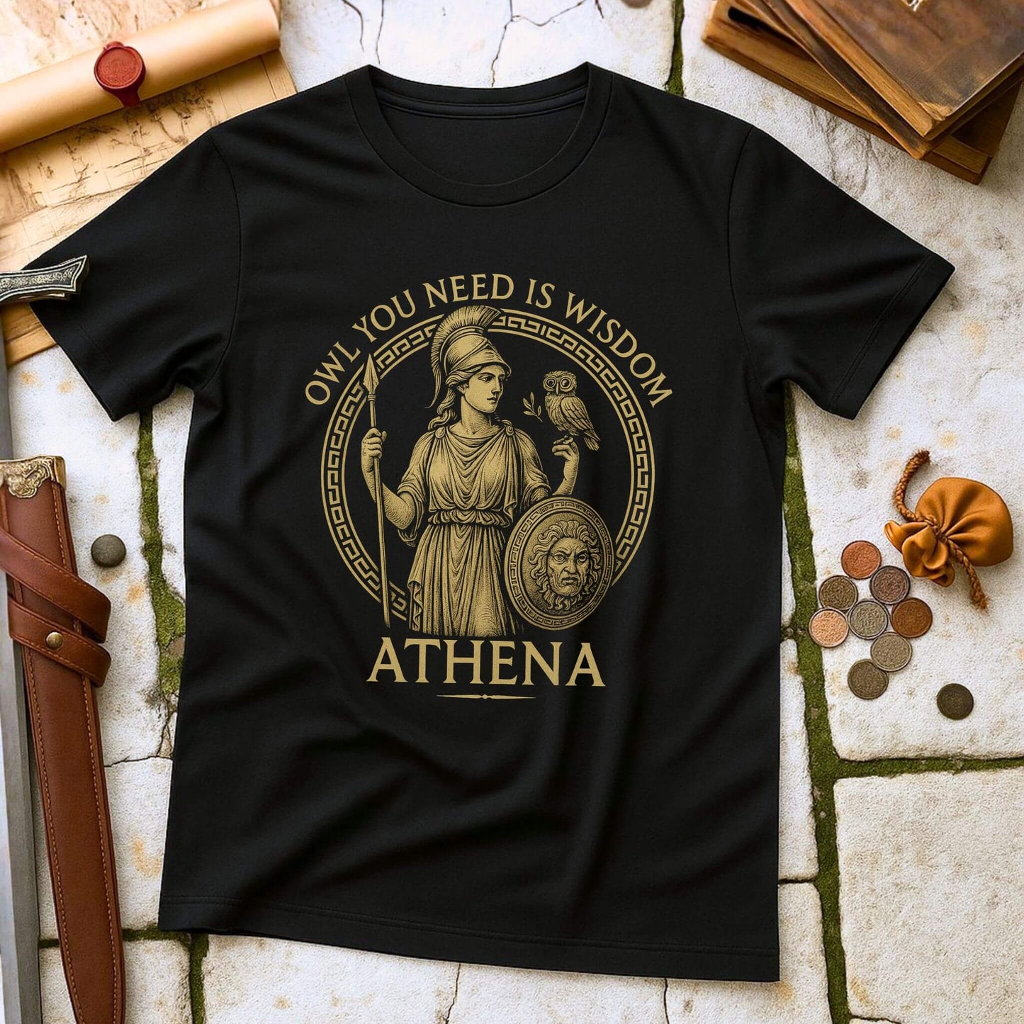 Black t-shirt with Athena graphic and text 'OWL YOU NEED IS WISDOM ATHENA' on a stone surface with classical items.