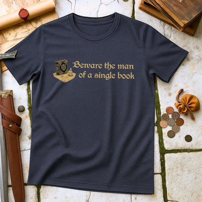 Heather navy t-shirt with 'Beware the man of a single book' text on a stone surface with books and coins.
