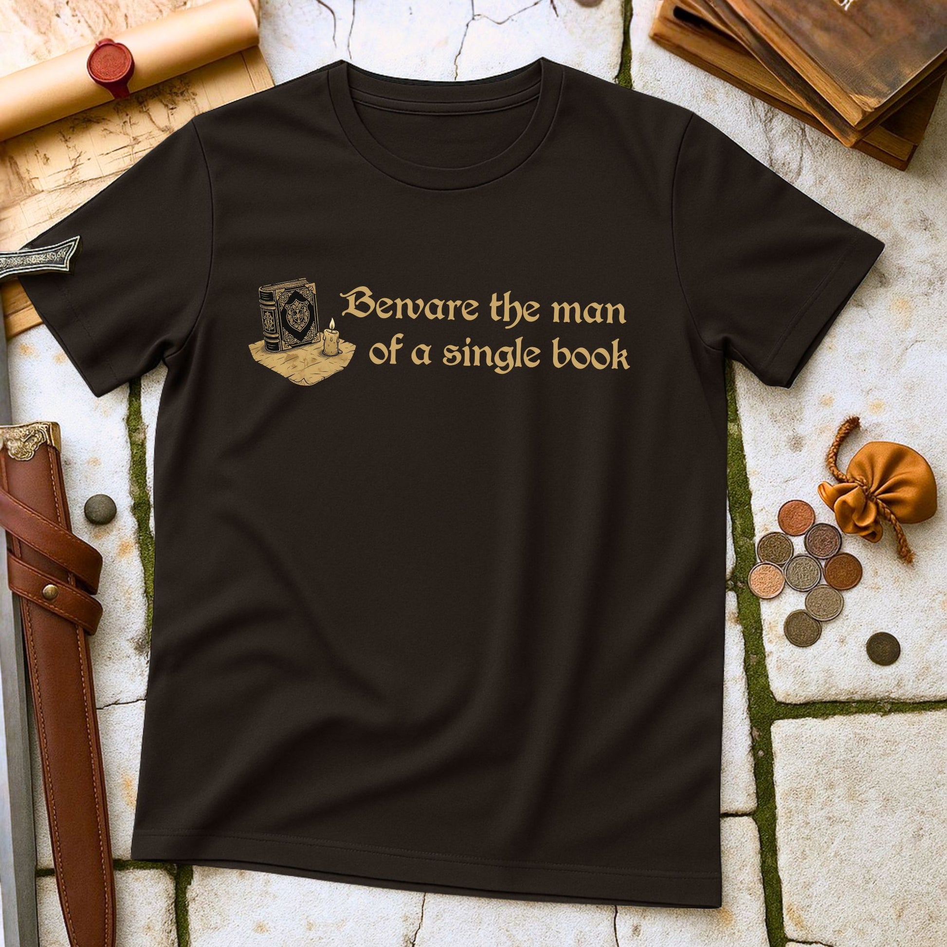 Black t-shirt with gold text and design on a textured surface with books and coins.