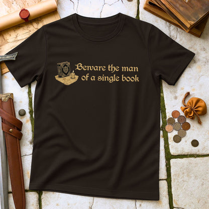 Black t-shirt with gold text and design on a textured surface with books and coins.