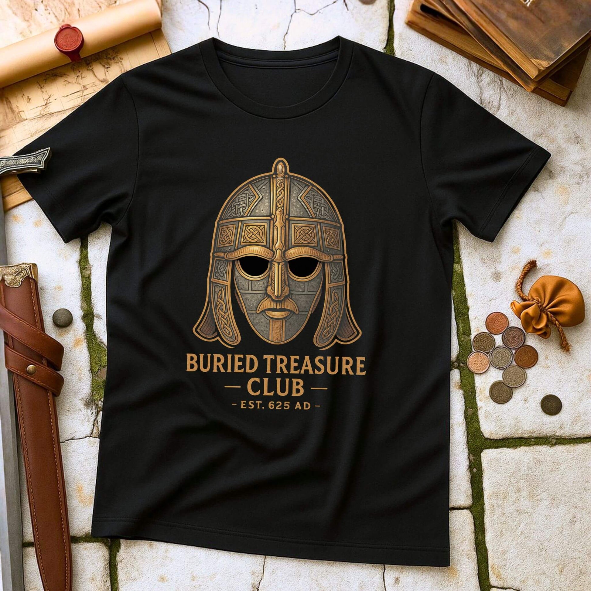 Black t-shirt with a Sutton Hoo helmet  graphic and 'Buried Treasure Club EST.625 AD' text on a stone surface