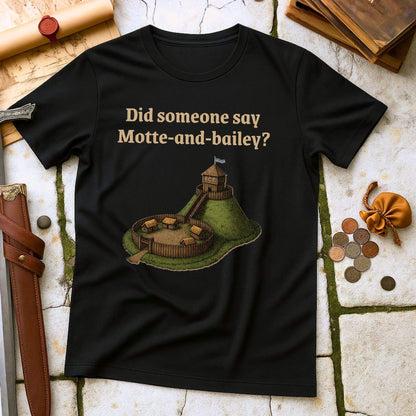 Black t-shirt with a graphic and text " Did someone say Motte and Bailey" on a stone surface with props.