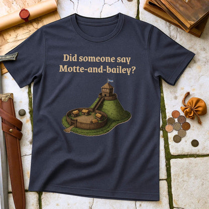 Heather Navy t-shirt with a graphic and text " Did someone say Motte and Bailey" on a stone surface with props.