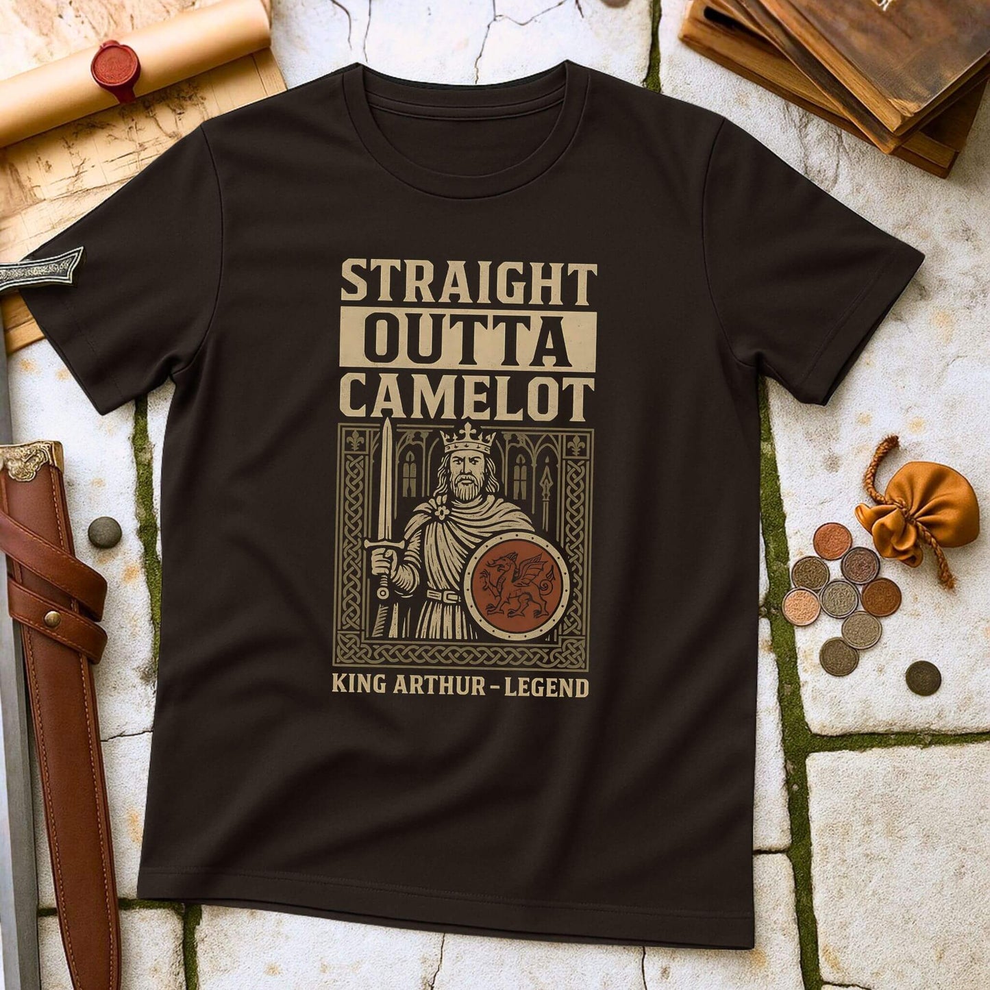 Dark Chocolate t-shirt with King Arthur graphic and 'Straight Outta Camelot' text on a stone surface with props.