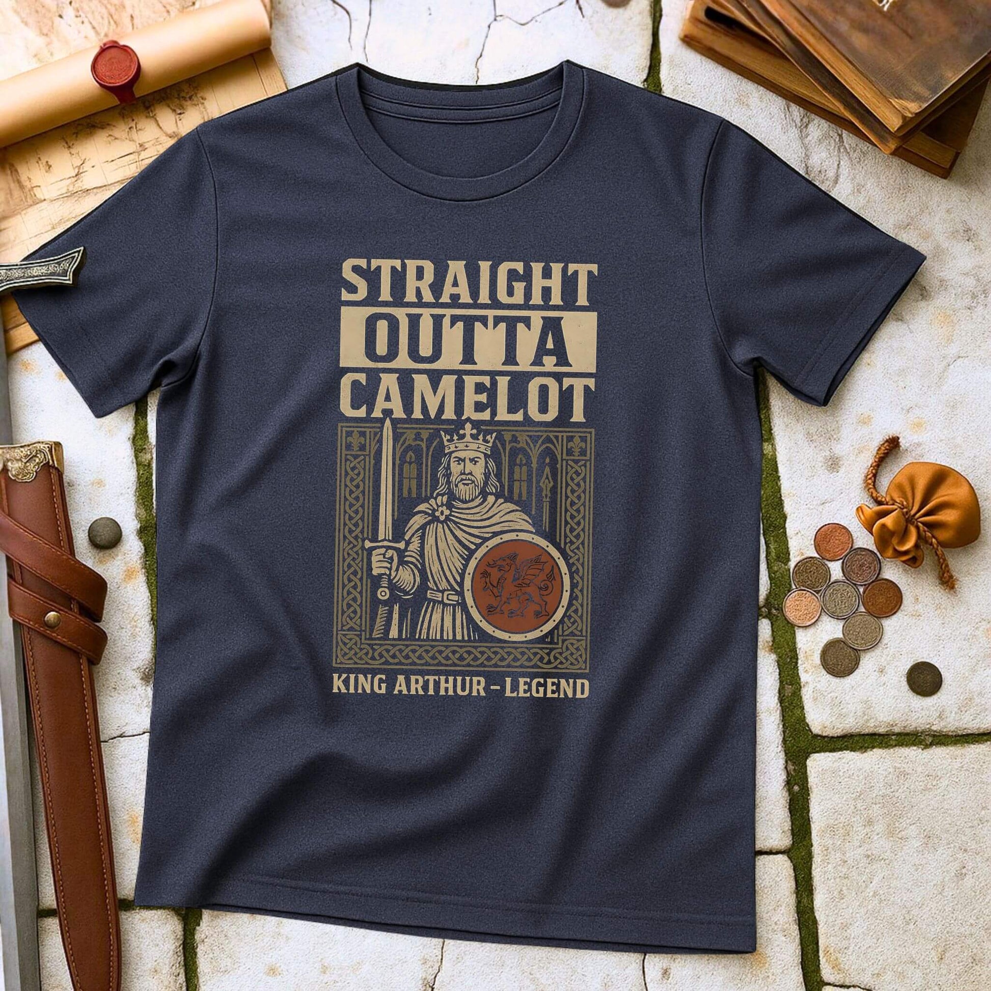 Heather Navy blue t-shirt with King Arthur graphic and 'Straight Outta Camelot' text on a stone surface with props.