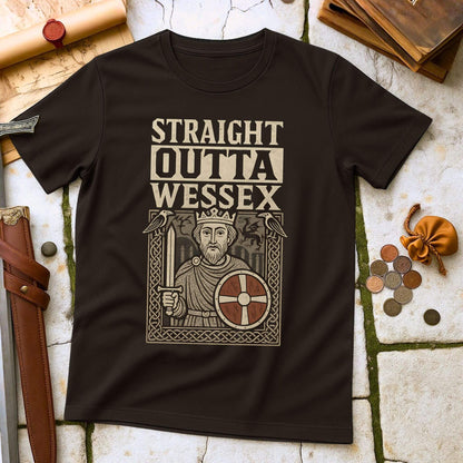 Dark Chocolate t-shirt mockup featuring a 'Straight Outta Wessex' design with King Alfred the Great holding a sword and shield, surrounded by Anglo-Saxon art, laid flat on a stone and leather historical background
