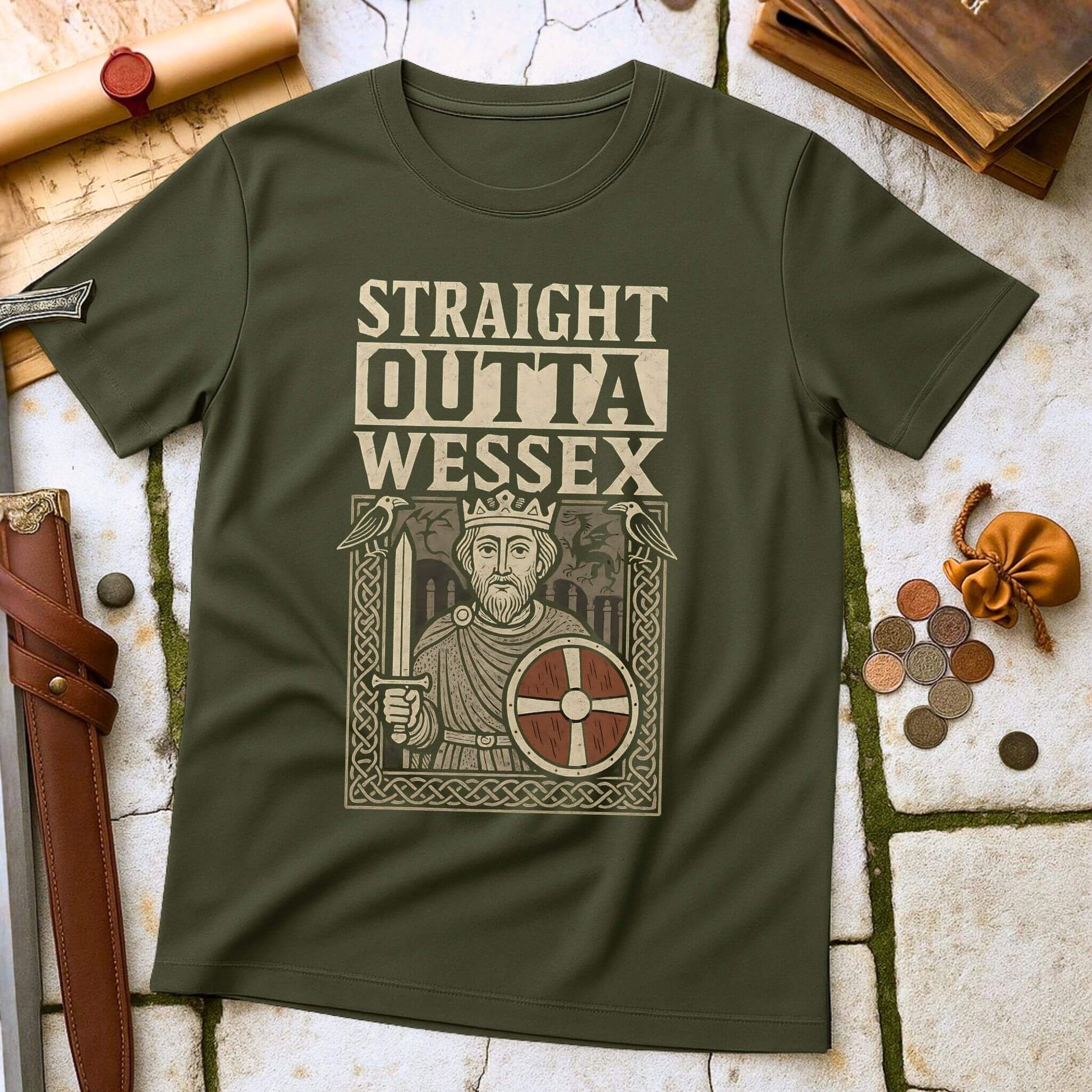 Military Green t-shirt mockup featuring a 'Straight Outta Wessex' design with King Alfred the Great holding a sword and shield, surrounded by Anglo-Saxon art, laid flat on a stone and leather historical background